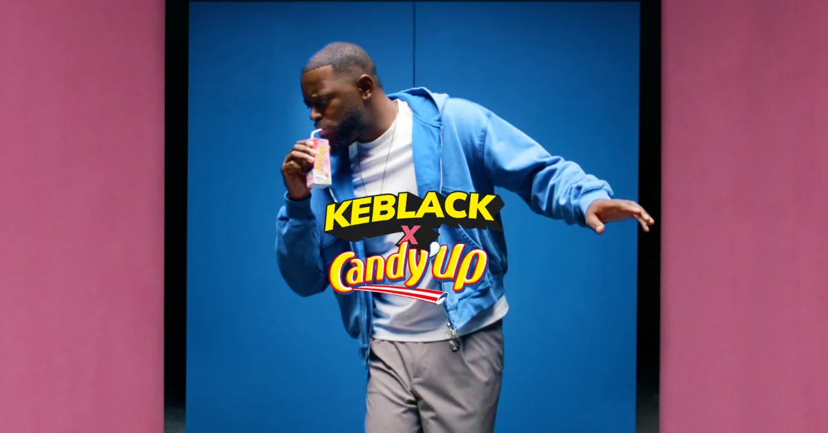 Capture du clip Pas normal interprété par Keblack pour la campagne Candy'Up signée 87seconds dévoilée le 12 juin 2026, le rappeur en sweat à capuche bleu siffle une brique de Candy'Up sur fond rose et bleu chromé, logos Keblack en jaune et Candy'Up en rouge surimprimés au centre, esthétique culture urbaine et pause goûter