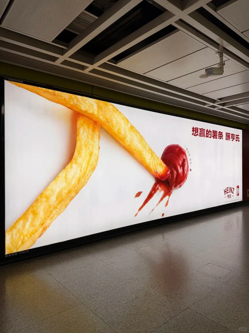 Affichage Heinz dans le métro de Canton (Guangzhou) pour la Coupe du Monde 2026, panneau lumineux montrant deux frites dessinant les jambes d'un footballeur en plein effort et une dose de ketchup formant le ballon, slogan en idéogrammes rouges sur fond blanc, campagne d'activation virale lancée le 11 juin 2026 jour de l'ouverture du Mondial