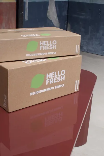 Photographie d'une seconde table mise en vente sur leboncoin dans le cadre de l'opération La Bonne Table by HelloFresh du 14 juin 2026, ancienne table de ferme en bois clair patiné par les ans posée dans un atelier de chineur du Sud-Ouest, plateau gravé de noms et de cœurs, chaises en paille tressée alignées autour, lumière naturelle d'après-midi