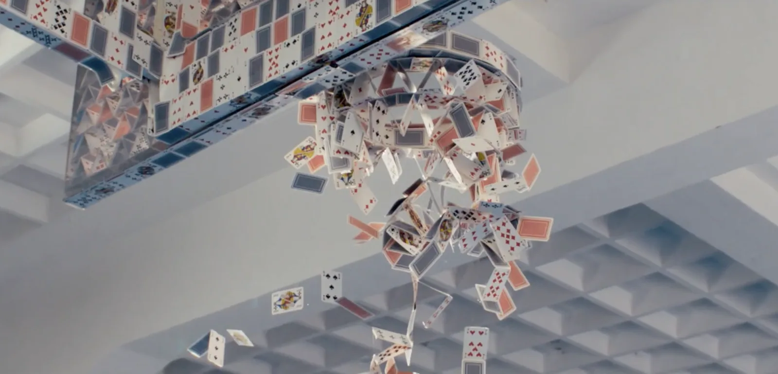 Image clé du film Avoir un temps d'avance de La Banque Postale dévoilé le 14 juin 2026, châteaux de cartes en suspension qui s'effondrent en pluie au-dessus d'une grande pièce blanche aux gradins capitonnés, métaphore de la fragilité des projets clients, maquettes réelles complétées en post-production 3D, réalisé par Nico Perez Veiga via Iconoclast, signé Saatchi Saatchi pour les 20 ans de la banque