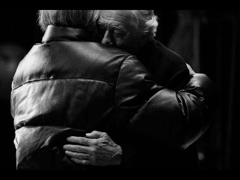 Photogramme bonus making-of de la campagne Warmer Together signée Wesayhi Sliema pour Moncler shooté par Platon à New York, plan rapproché en noir et blanc d'Al Pacino et Robert De Niro habillés en doudounes Moncler s'enlaçant longuement de profil, têtes posées contre l'épaule l'un de l'autre, mains visibles dans le dos, atmosphère intime de studio en très faible profondeur de champ