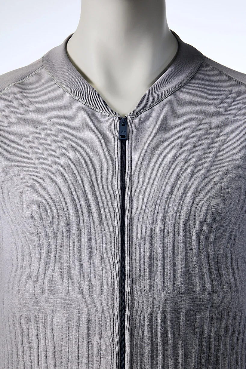 Détail technique de la Liquid Cooling Garment Prada Axiom dévoilée le 16 juin 2026, gros plan sur le réseau de tubes transparents tissés dans le textile blanc à hauteur du genou de l'astronaute, jonction en titane des conduits d'arrivée et de sortie d'eau visible, broderie Prada Sport discrète en argent sur la couture latérale, image studio en lumière naturelle