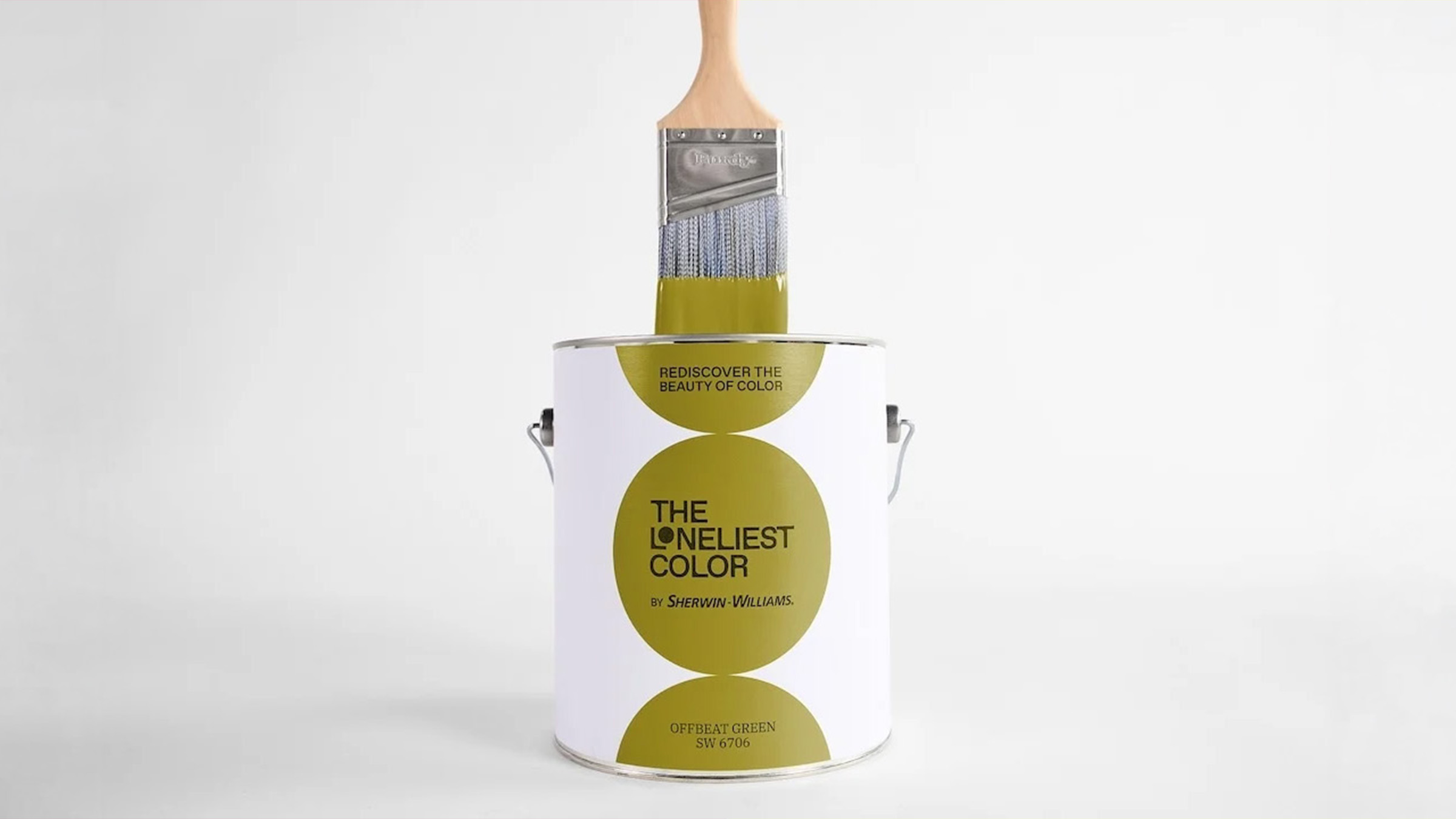 Photographie de studio sur fond blanc cassé du pot édition limitée The Loneliest Color 2026 signé Sherwin-Williams dévoilé le 10 juillet 2026, pot cylindrique métallique blanc à anse métallique portant l'étiquette design composée de trois cercles chartreuse olive alignés verticalement au centre desquels s'affichent en noir les mentions Rediscover the beauty of color en haut The Loneliest Color by Sherwin-Williams au centre et Offbeat Green SW 6706 en bas, un large pinceau Purdy en bois clair plongé dans le pot avec les poils enduits d'une épaisse couche de peinture chartreuse dégoulinant sur le bord, éclairage doux tirage e-commerce