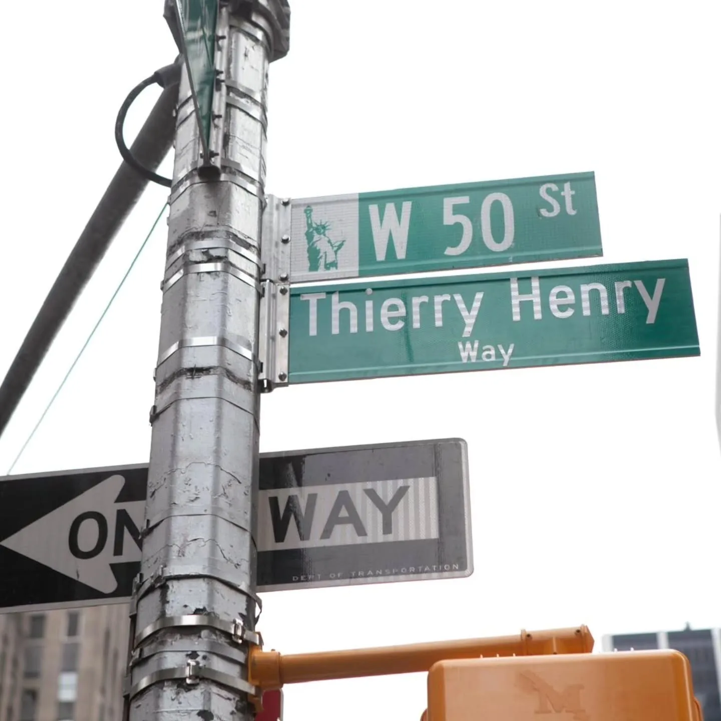 Plaque de rue Thierry Henry Way inaugurée le 12 juin 2026 à l'intersection de West 50th Street et 6th Avenue à Manhattan, panneau bleu marine et lettrage blanc accroché sous le panneau original West 50 ST, dispositif officiel temporaire signé par la municipalité de New York pour la Coupe du Monde 2026, à l'initiative de la conseillère Virginia Maloney et du maire Zohran Mamdani supporter d'Arsenal